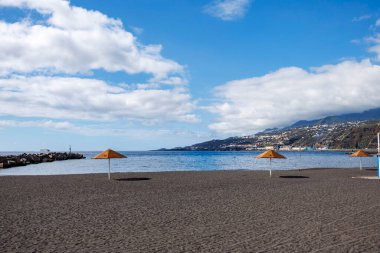 Turuncu şemsiyeli geniş kumlu sahil ve açık mavi gökyüzünün altında boş kıyı şeridi. Yazın başlarındaki sessiz beklentileri simgeliyor..