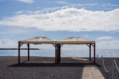 Deniz kenarındaki boş bir gölgeliğe giden ahşap yolu olan simetrik plaj sahnesi, yaz başlamadan önce dinginliği ifade ediyor..