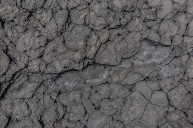 Doğal yarıklar ve katmanlı dokularla parçalanmış volkanik taş yüzeyinin detaylı yakın çekimi jeolojik temalar veya soyut tasarım arka planları için idealdir.