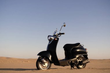 Günbatımında Namib Çölü 'nün altın kumunda siyah bir scooter.