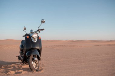 Günbatımında Namib Çölü 'nün altın kumunda siyah bir scooter.