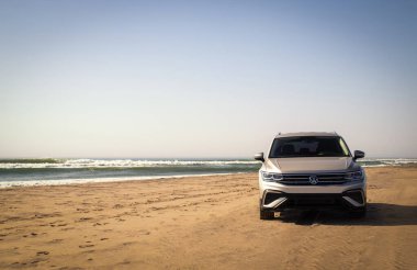 Gri Volkswagen Tiguan Namib Çölü 'nün kıyı şeridinde parlak bir gökyüzünde. Walvis Körfezi, Namibya. 