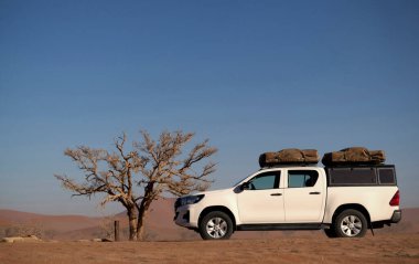 Güneşli bir günde Namib Çölü 'nün kırmızı kumlarında beyaz bir off-road arabası duruyor. Sossusvlei, Namibya
