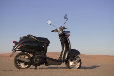 Günbatımında Namib Çölü 'nün altın kumunda siyah bir scooter.