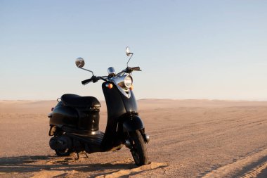 Günbatımında Namib Çölü 'nün altın kumunda siyah bir scooter.