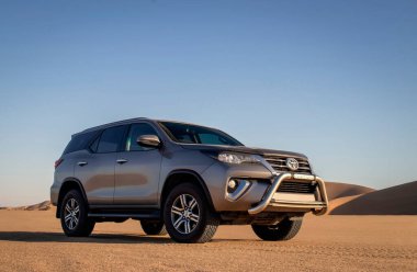 Namib Çölü 'nün ortasında parlak bir gökyüzüne karşı gri bir Toyota Fortuner.