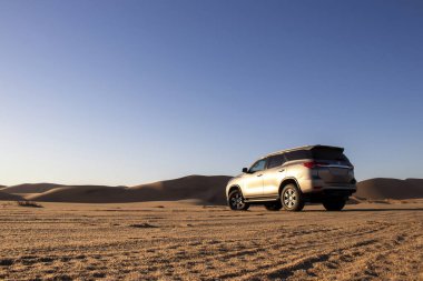 Namib Çölü 'nün ortasında parlak bir gökyüzüne karşı gri bir Toyota Fortuner.