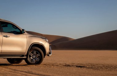 Namib Çölü 'nün ortasında parlak bir gökyüzüne karşı gri bir Toyota Fortuner.