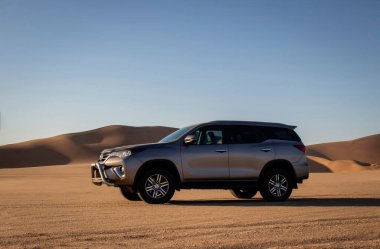 Gri Toyota Fortuner Namib Çölü 'nün kum tepelerine karşı gün batımında. Büyüleyici bir sahne. Macera, keşif ve engin altın manzaranın güzelliği.