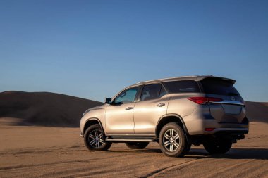 Gri Toyota Fortuner Namib Çölü 'nün kum tepelerine karşı gün batımında. Büyüleyici bir sahne. Macera, keşif ve engin altın manzaranın güzelliği.