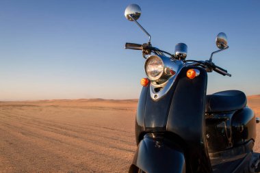 Günbatımında Namib Çölü 'nün altın kumunda siyah bir scooter.