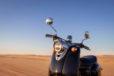 Günbatımında Namib Çölü 'nün altın kumunda siyah bir scooter.