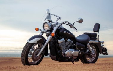 Namib Çölü 'nün kumlu yüzeyinde dramatik bulutlu bir gökyüzüne karşı tek başına duran bir motosiklet. Günbatımı ışığı, doğayla makine arasındaki zıtlığı vurgular..