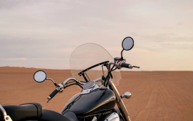 Namib Çölü 'nün kumlu yüzeyinde dramatik bulutlu bir gökyüzüne karşı tek başına duran bir motosiklet. Günbatımı ışığı, doğayla makine arasındaki zıtlığı vurgular..