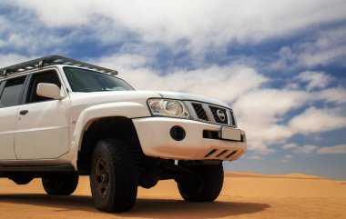 Uçsuz bucaksız Namib Çölü 'nde maceraya hazır beyaz bir SUV, üzerimizde kasvetli bir gökyüzü, keşif ve dayanıklılık ruhunu yakalıyor..