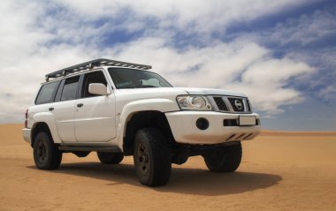 Uçsuz bucaksız Namib Çölü 'nde maceraya hazır beyaz bir SUV, üzerimizde kasvetli bir gökyüzü, keşif ve dayanıklılık ruhunu yakalıyor..