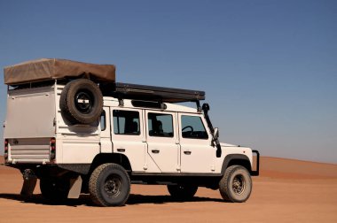 Güneşli bir günde Namib Çölü 'nün kırmızı kumlarında bir off-road arabası duruyor. Sossusvlei, Namibya. Afrika