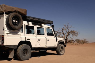 Güneşli bir günde Namib Çölü 'nün kırmızı kumlarında bir off-road arabası duruyor. Sossusvlei, Namibya. Afrika