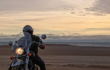 Gün batımında motosikletli bir adamın gerçek fotoğrafı dramatik bulutlar içinde özgürlük, seyahat, yalnızlık, macera ve açık arazide açık hava yaşam tarzı kavramı.