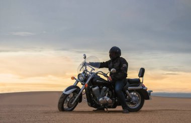 Gün batımında motosikletli bir adamın gerçek fotoğrafı dramatik bulutlar içinde özgürlük, seyahat, yalnızlık, macera ve açık arazide açık hava yaşam tarzı kavramı.