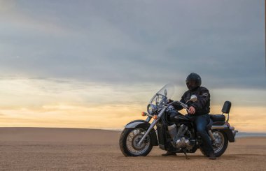 Gün batımında motosikletli bir adamın gerçek fotoğrafı dramatik bulutlar içinde özgürlük, seyahat, yalnızlık, macera ve açık arazide açık hava yaşam tarzı kavramı.
