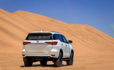 Parlak bir yaz gününde Namib Çölü 'nün kumullarında beyaz bir Toyota Fortuner.