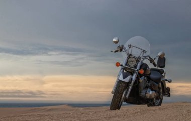 Bir motosiklet, gün batımının altında hareketsiz durur. Özgürlüğü, macerayı ve önümüzde yeni yollar keşfetmenin heyecanını sembolize eder..