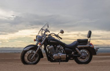 Bir motosiklet, gün batımının altında hareketsiz durur. Özgürlüğü, macerayı ve önümüzde yeni yollar keşfetmenin heyecanını sembolize eder..