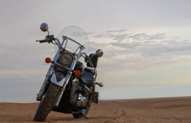 Bir motosiklet, gün batımının altında hareketsiz durur. Özgürlüğü, macerayı ve önümüzde yeni yollar keşfetmenin heyecanını sembolize eder..