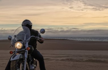 Gün batımında motosikletli bir adamın gerçek fotoğrafı dramatik bulutlar içinde özgürlük, seyahat, yalnızlık, macera ve açık arazide açık hava yaşam tarzı kavramı.