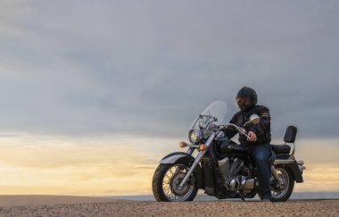 Gün batımında motosikletli bir adamın gerçek fotoğrafı dramatik bulutlar içinde özgürlük, seyahat, yalnızlık, macera ve açık arazide açık hava yaşam tarzı kavramı.