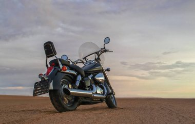 Bir motosiklet, gün batımının altında hareketsiz durur. Özgürlüğü, macerayı ve önümüzde yeni yollar keşfetmenin heyecanını sembolize eder..