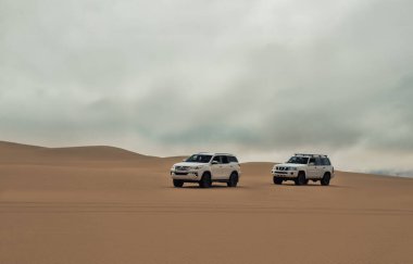 Çöldeki yüksek kum tepelerinin içinden geçen 4x4 'lük bir grup araç enerji, sıcaklık ve macera dolu güçlü güneş ışığı açıklarında toz kaldırıyor.