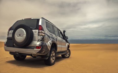 Gücün varlıkla buluştuğu gerçek fotoğraf. Bu gri SUV kumların üzerinde duruyor, fırtınalı bir gökyüzü tarafından çerçevelenmiş özgürlüğün cesur bir sembolü, cesaret ve vahşi doğada durdurulamaz bir güç.