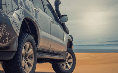 Gücün varlıkla buluştuğu gerçek fotoğraf. Bu gri SUV kumların üzerinde duruyor, fırtınalı bir gökyüzü tarafından çerçevelenmiş özgürlüğün cesur bir sembolü, cesaret ve vahşi doğada durdurulamaz bir güç..