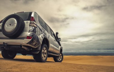 Gücün varlıkla buluştuğu gerçek fotoğraf. Bu gri SUV kumların üzerinde duruyor, fırtınalı bir gökyüzü tarafından çerçevelenmiş özgürlüğün cesur bir sembolü, cesaret ve vahşi doğada durdurulamaz bir güç..