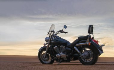 Bir motosiklet, gün batımının altında hareketsiz durur. Özgürlüğü, macerayı ve önümüzde yeni yollar keşfetmenin heyecanını sembolize eder..