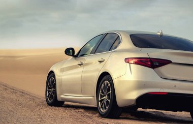  Tozlu bir Namibya yolunda, engebeli çöl arazisiyle modern tasarımı harmanlayan gümüş renkli bir araç görüldü. Seyahat, otomotiv ve editoryal temalar için ideal. 