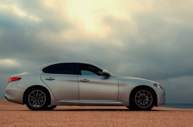  Tozlu bir Namibya yolunda, engebeli çöl arazisiyle modern tasarımı harmanlayan gümüş renkli bir araç görüldü. Seyahat, otomotiv ve editoryal temalar için ideal. 