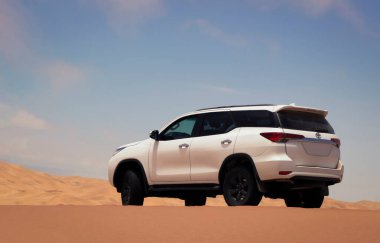 Beyaz bir Toyota Fortuner Namib Çölü 'nün altın tepelerinin arasına park etmiş, parlak yaz güneşinin altında parlıyor. Off-road özgürlüğünün ve engebeli zarafetin cesur bir sembolü.. 