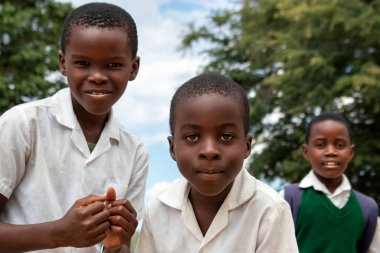 Üniformalı neşeli Afrikalı öğrencilerin birinci sınıf yakın çekimi. Doğal ışık altında gülümsüyorlar. Gerçek hayatta gençliği, eğitimi, mutluluğu ve kültürel canlılığı yakalıyorlar..