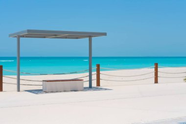 Sahilde modern ahşap banklı plaj gölgesi çadırı. Saadiyat Adası, Birleşik Arap Emirlikleri 'nde turkuaz suyu bulunan beyaz kumlu plaj..