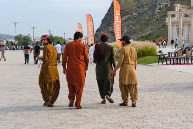 Khor Fakkan, Sharjah, UAE - Apr 10, 2024: Back view of group of 4 young poor middle eastern migrant men wearing colorful traditional casual cloth walking on the streets for Eid Al Fitr vacation clipart