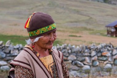 Sibirya, Altai, Rusya, 9 Ağustos, 2024. Altai etnik kökenli yaşlı bir kadının açık hava portresi, bulanık doğal arka plan üzerine yerel ulusal elbise ve şapka giyiyor.