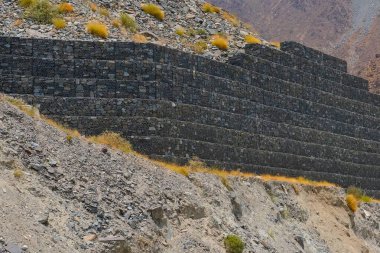 Dağ yamacını metal ağlar ve taş bloklarla güçlendirmek gabion duvarlar, kayaların düşmesini önlemek, yolda dökülmesini önlemek. BAE 'de heyelan, kayalık erozyon kontrolü ve kaya kayması önleme