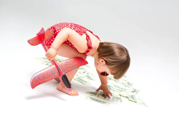 带着玩具飞机的小女孩从地板上拿起美元钞票 这些钞票被白色的背景隔开了 度假和旅行概念 — 图库照片