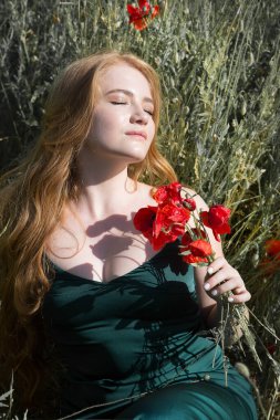 Young beautiful woman is resting lying in the grass on the field with a bouquet of poppies.