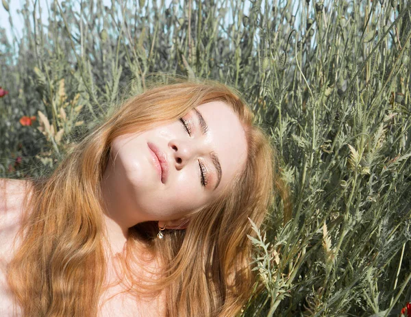 stock image Young beautiful woman is resting in the rays of the sun lying in the grass on the field.