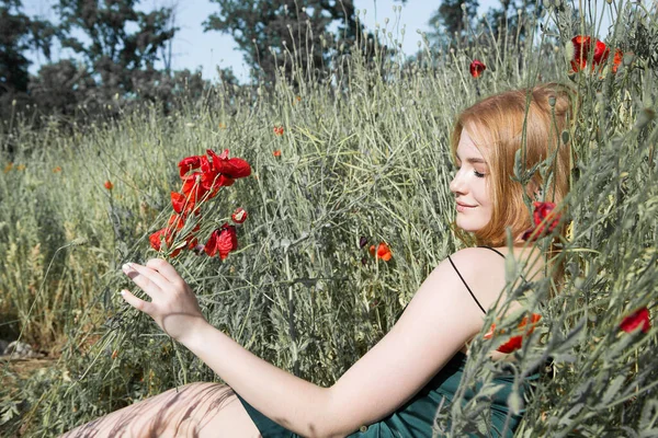 stock image Young beautiful woman is resting lying in the grass on the field with a bouquet of poppies.