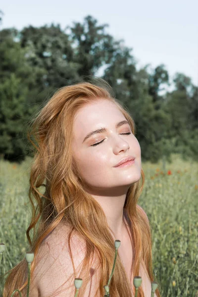 stock image Young beautiful woman is resting in the rays of the sun sitting in the grass on the field.